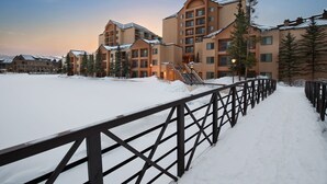 Area esterna innevata con recinto in legno, edifici con numerose finestre e una scala che conduce a un piano superiore.
