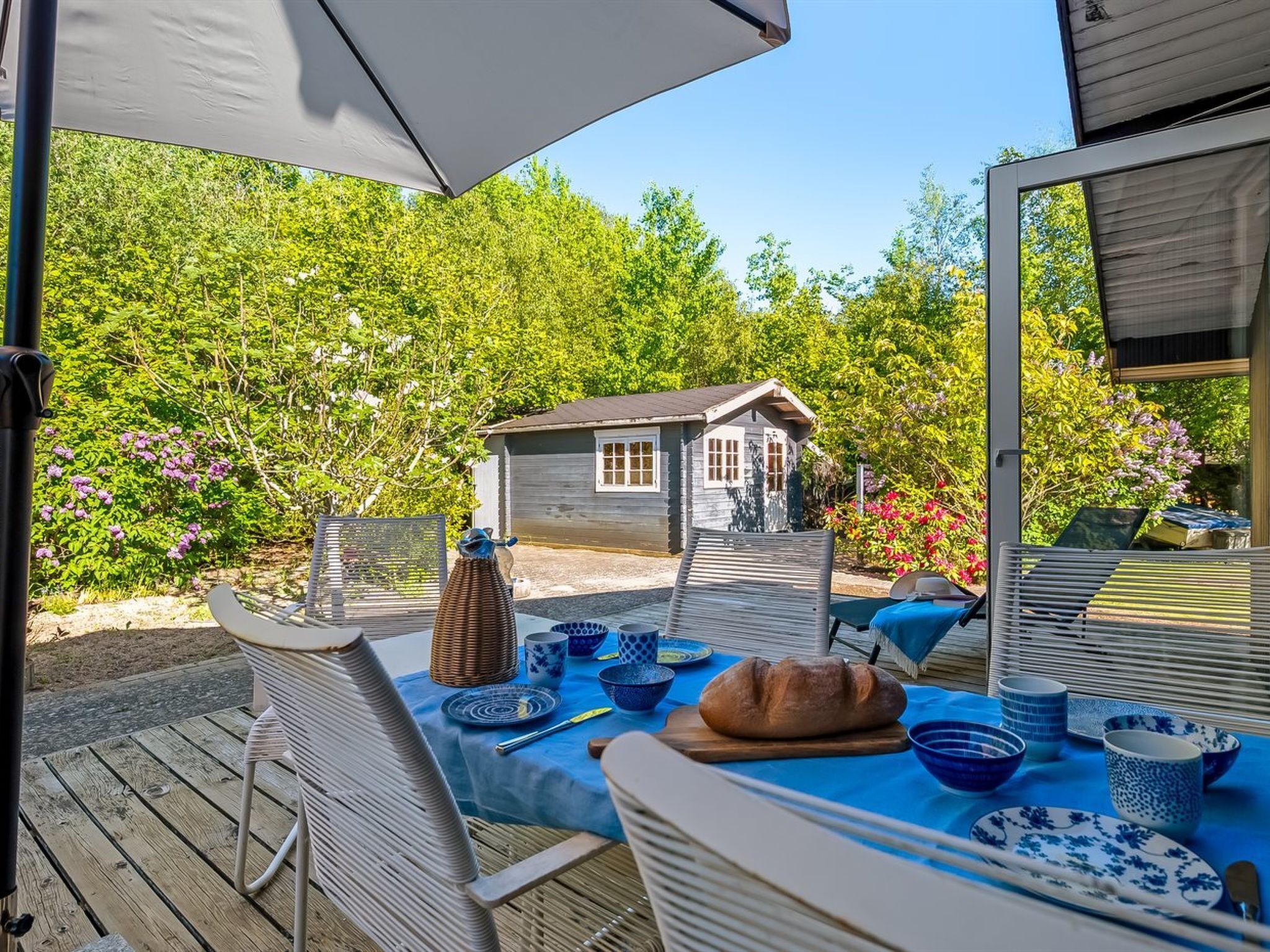 Ein Essbereich im Freien mit einem Tisch für zwei Personen, umgeben von Stühlen, einer kleinen Gartenhütte und üppigem Grün.