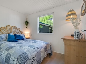 Ein Schlafzimmer mit einem Bett, einem Fenster, einer Nachttischlampe, einer hängenden Pflanze und einer Holzkommode.