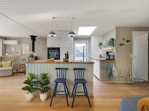 Eine moderne Küche mit einer zentralen Kochinsel, Barhocker und einem Essbereich mit einer Couch und Stühlen.