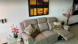 Un salon moderne avec un canapé, des coussins décoratifs, une œuvre d’art murale et une petite table sur laquelle est posé un vase de fleurs.