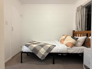 A single bed with a checkered blanket, two pillows, a wooden headboard, and a white wardrobe. - 3BR Home - Walk to Train, Lynn Mall & Westgate (Auckland)