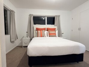A bedroom with a bed, curtains, a window, a nightstand, and a wardrobe. - 3BR Home - Walk to Train, Lynn Mall & Westgate (Auckland)