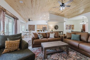 Ein geräumiges Wohnzimmer mit einem braunen Ledersofa, einem Holztisch und einem Deckenventilator.