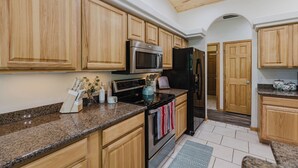 Una cocina con armarios de madera, encimeras de granito, electrodomésticos de acero inoxidable y suelo de baldosas.