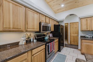 Eine Küche mit Holzschränken, Granit Arbeitsplatten, Edelstahlgeräten und Fliesenboden.