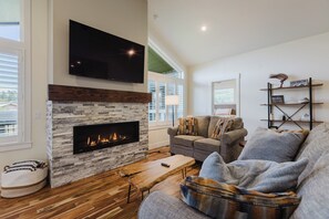 A living room with a fireplace, a flat-screen TV, a sofa, and a bookshelf. - 3BR Pet-Friendly Home | Fire Table, Fenced Yard + PLPOA Lake Access (Pagosa Springs)
