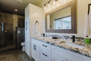 A bathroom with a large mirror, a sink, and a shower area. - 3BR Pet-Friendly Home | Fire Table, Fenced Yard + PLPOA Lake Access (Pagosa Springs)
