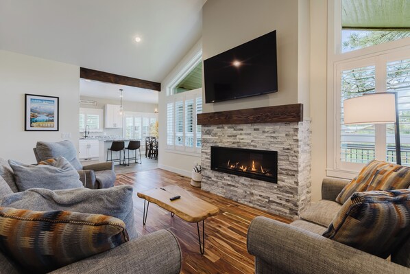 A living room with a fireplace, a television mounted above it, and a dining area in the background. - 3BR Pet-Friendly Home | Fire Table, Fenced Yard + PLPOA Lake Access (Pagosa Springs)