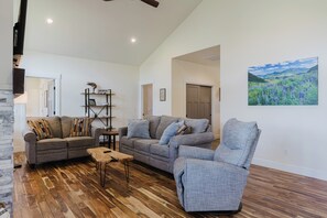 A spacious living room with a wooden floor, grey sofas, and a painting of a landscape. - 3BR Pet-Friendly Home | Fire Table, Fenced Yard + PLPOA Lake Access (Pagosa Springs)