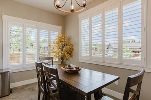 A dining area with a wooden table, chairs, a vase with flowers, and large windows with blinds. - 3BR Pet-Friendly Home | Fire Table, Fenced Yard + PLPOA Lake Access (Pagosa Springs)