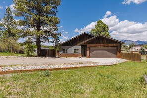 A single-story house with a garage, surrounded by a gravel driveway and a wooden fence. - 3BR Pet-Friendly Home | Fire Table, Fenced Yard + PLPOA Lake Access (Pagosa Springs)