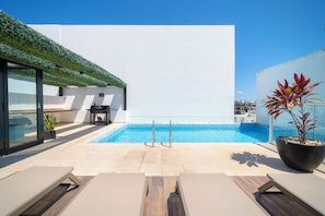 A rooftop pool with lounge chairs, a potted plant, and a clear blue sky.