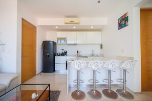 A modern kitchen with white cabinets, a black refrigerator, and a bar area with white stools.