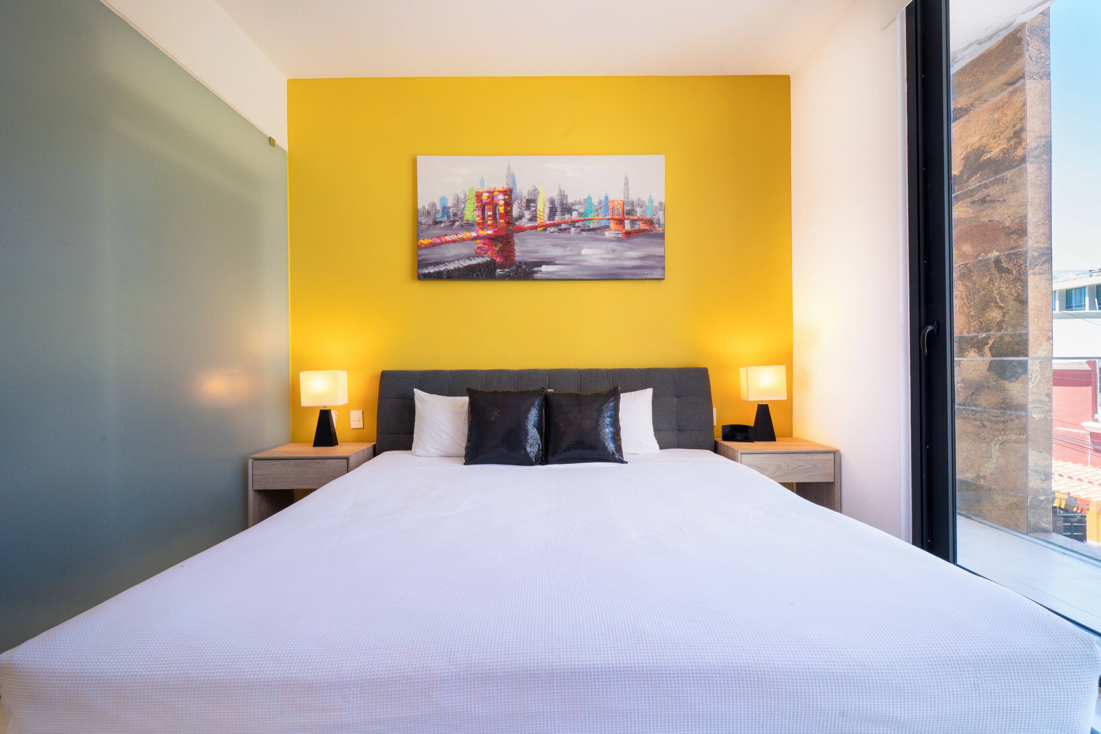 A hotel room with a large bed, two bedside tables with lamps, a painting on the wall, and a window.