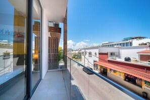 A balcony with a glass railing overlooking a street with shops and buildings.