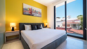 A modern hotel room with a large bed, two bedside tables with lamps, a cityscape painting on the wall, and a large window offering a view of buildings. - Apartment with Balcony & Pool (Playa del Carmen)