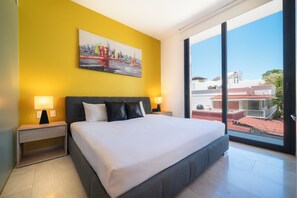 Ein modernes Hotelzimmer mit einem großen Bett, zwei Nachttischen mit Lampen, einem Stadtbild an der Wand und einem großen Fenster mit Blick auf Gebäude.