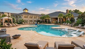 A pool area with lounge chairs, a fire pit, and a building with a tower. - Families favorite Luxury Suites + Saltwater Pool+Gym + Free Parking+Ev Charging (Matthews)