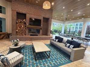 A modern living room with a brick fireplace, a flat-screen TV, a sofa, and a coffee table. - Families favorite Luxury Suites + Saltwater Pool+Gym + Free Parking+Ev Charging (Matthews)