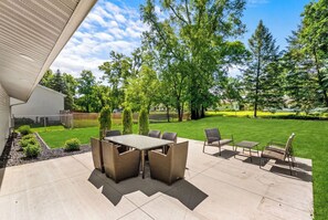 Eine Terrasse mit Tisch und Stühlen, umgeben von einer Rasenfläche und Bäumen.