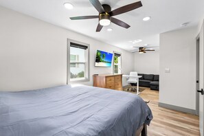 Ein Schlafzimmer mit Bett, Schreibtisch, Stuhl, Sofa, Deckenventilator und Fenster.