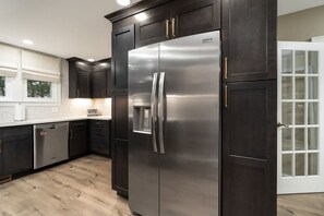 A modern kitchen with dark cabinetry, stainless steel appliances, and a window with blinds. - Riverside Retreat Vacation Home (West Lafayette)