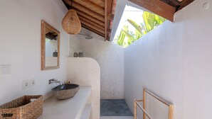 Uma casa de banho moderna com lavatório de pedra, espelho com moldura de madeira, cesto trançado e banco de madeira.