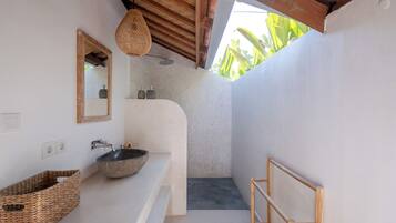 A modern bathroom with a stone sink, a wooden-framed mirror, a woven basket, and a wooden bench.