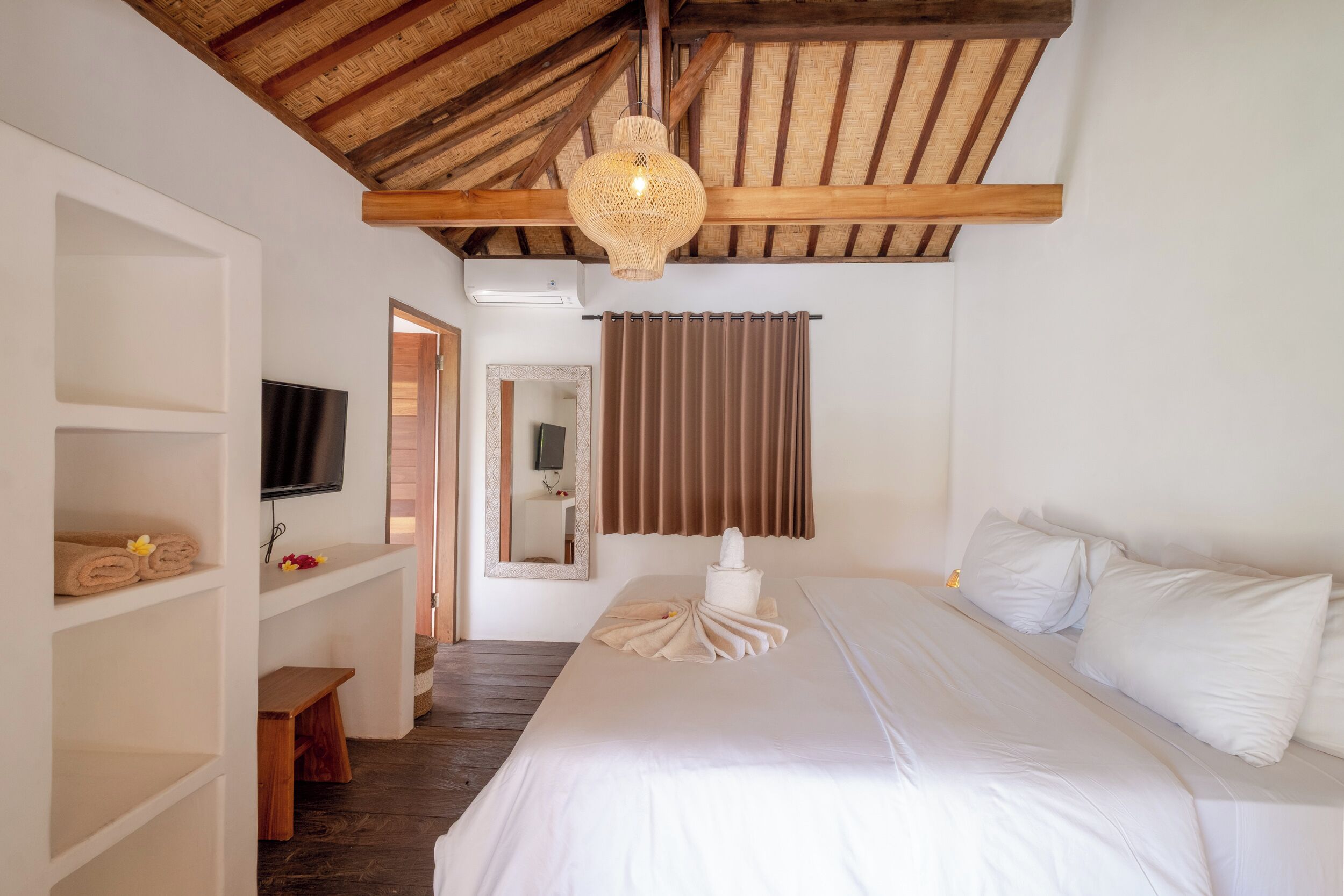 Ein Schlafzimmer mit Holzboden, einem Bett mit weißer Bettwäsche, einem Fernseher an der Wand und einem Spiegel.