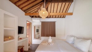 Quarto com teto de madeira, cama com roupa de cama branca, televisão na parede e um espelho.
