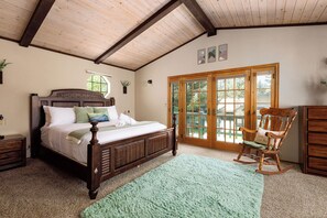 A bedroom with a wooden bed, a rocking chair, a green rug, and a sliding glass door to the outside. - Teakwood Chalet - Games / Fire Pit / Minutes to Lake and Ski (Big Bear Lake)