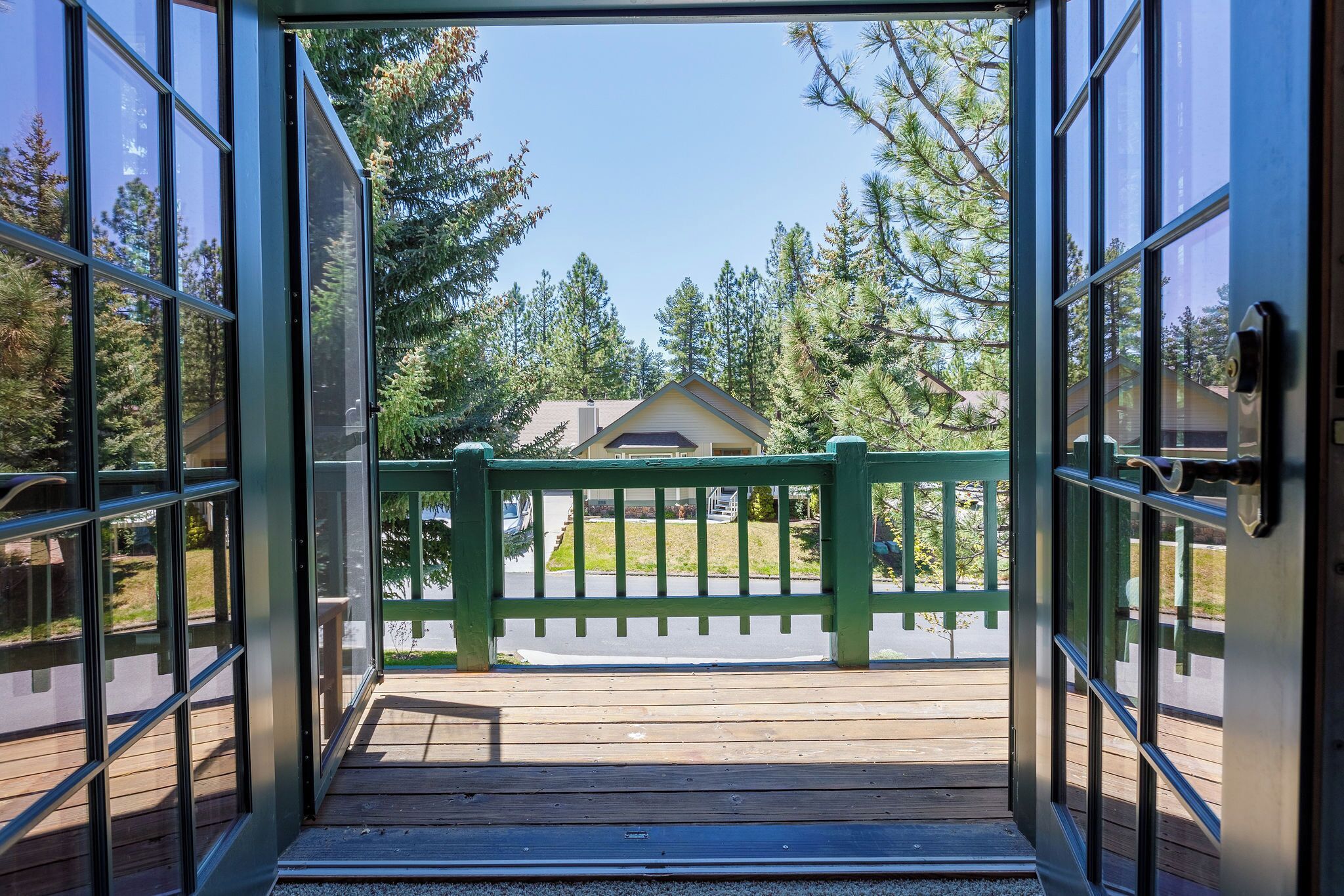 An open door leading to a wooden deck with a green railing, overlooking a residential area with houses and trees.