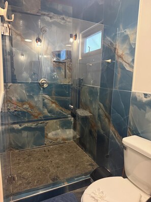 Et badeværelse med en brusekabine med glasvægge, toilet og væg i marmor.