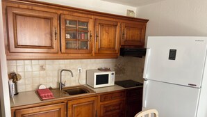 Een keuken met houten kastjes, een magnetron, een spoelbak en een koelkast.