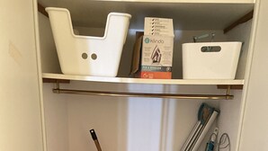 Een inpandige kast met planken vol schoonmaakartikelen, waaronder een stofzuiger, dweilen en schoonmaakbakken.
