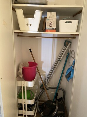 Ein Stauraum mit Regalen, auf denen Reinigungsmittel, darunter ein Staubsauger, Wischmopps und Reinigungsbehälter, gelagert sind.