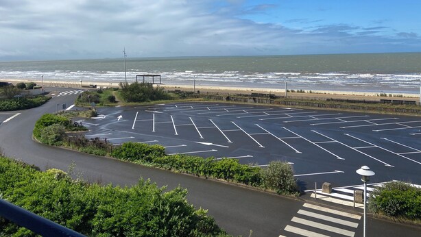 Een parkeerplaats met duidelijke rijstroken, een voetgangersoversteek en uitzicht op het strand en de oceaan.