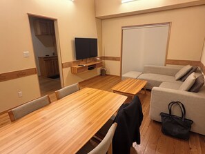Ein Zimmer mit Holztisch, einer Couch, einem an der Wand montierten Fernseher und einer Schiebetür.