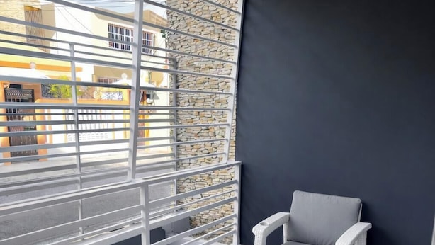 Un balcone con mobili in vimini bianco, una sedia imbottita di grigio e un muro in pietra.
