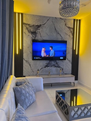 A modern living room with a marble wall, a flat-screen TV, a sofa, and a glass coffee table.