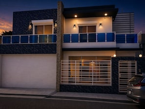 A modern two-story building with a garage, a balcony, and a car parked in front.