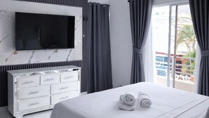 Una camera d'albergo moderna con un letto, una televisione a schermo piatto fissata a una parete in marmo, una cassettiera bianca e un balcone con tende.