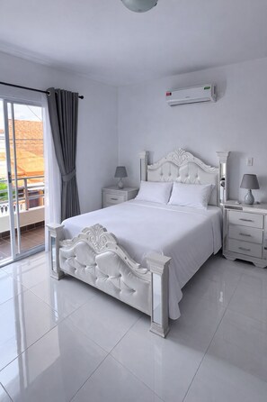 A white bedroom with a large bed, two bedside tables, a window with curtains, and a ceiling fan.