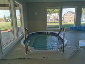 A hot tub with metal railings, large windows, and a view of a residential area.