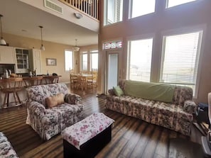 A spacious living room with a floral sofa, a matching ottoman, and a dining area with wooden furniture.