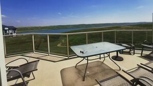 Ein Balkon mit Glastisch und Stühlen, mit Blick auf einen See und eine grüne Landschaft.