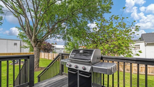 En trädgård med en Genesis-grill, ett trädäck, ett träd och ett trästaket.