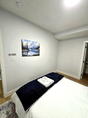 Une chambre à coucher avec un lit, un tableau représentant un paysage de montagne, un panneau « Il est interdit de fumer » et une porte.
