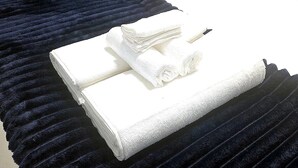 Un letto rifatto con cura, una coperta blu scuro, un mucchio di asciugamani bianchi e un comodino con una lampada.